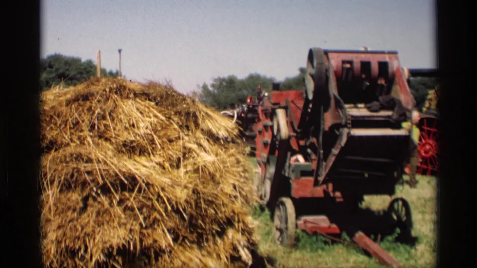 1969 Mabel, Minnesota 8mm frame of a straw pile and red thresher from a close handheld field viewpoint, with small people near the equipment.