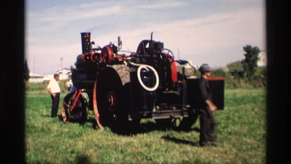 A large red and black steam tractor is displayed on grass as several men observe in Mabel, Minnesota in 1969.