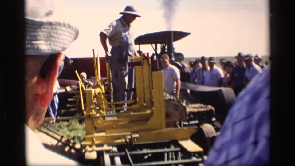 A man stands on yellow tracked agricultural machinery while a crowd watches at the 1969 rural exhibition in Mabel, Minnesota.