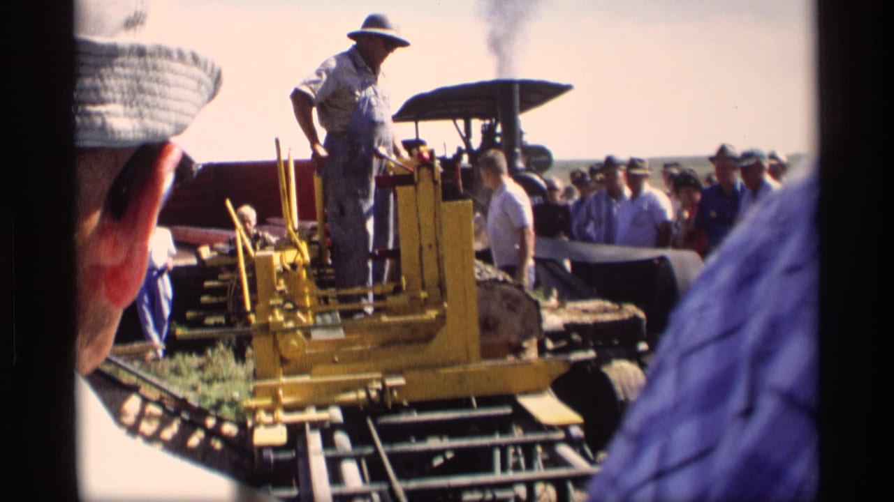 1969 Mabel, Minnesota home-movie frame showing a man on a yellow wood-cutting machine with logs, smoke, and a crowd around him.
