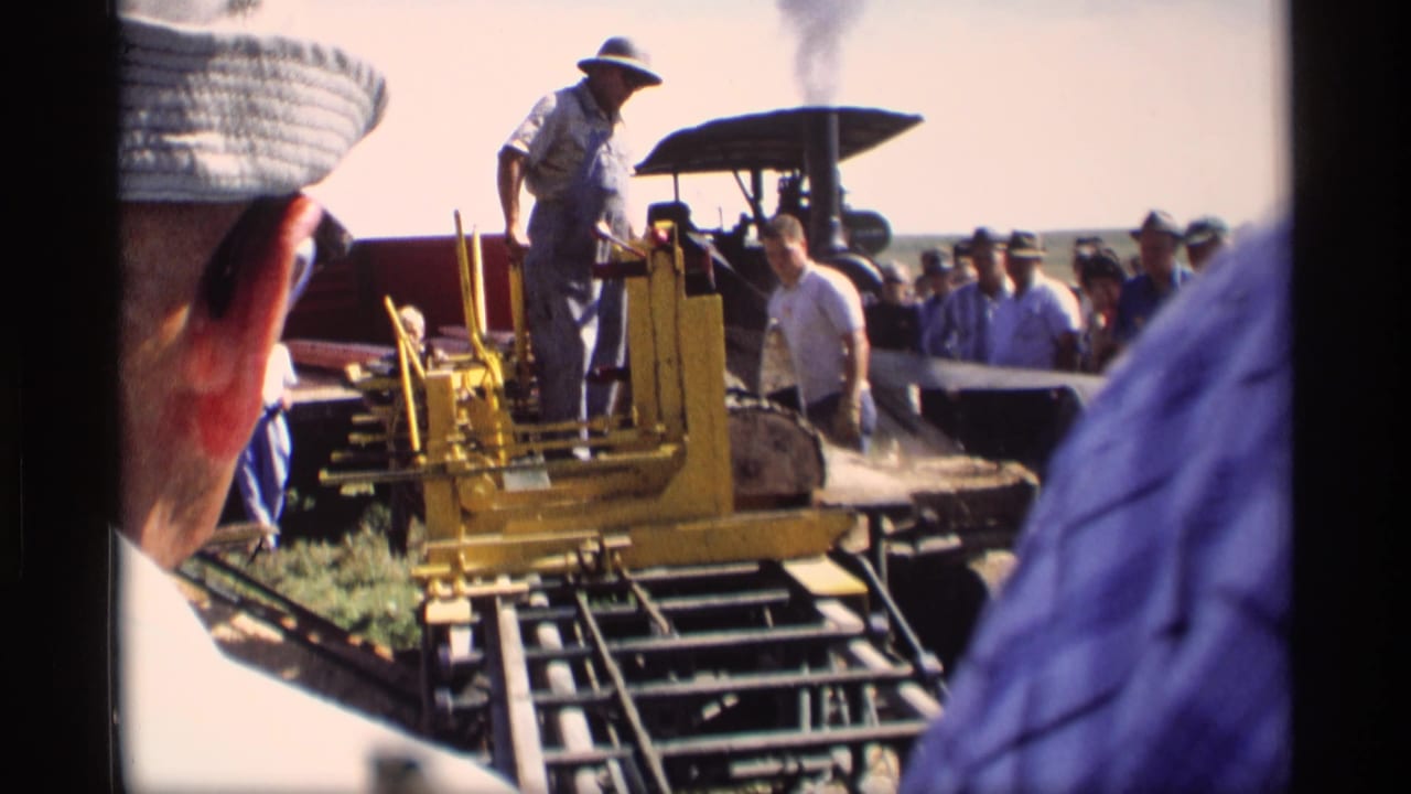 Crowd surrounds a yellow wood-cutting machine with an operator standing above the controls.