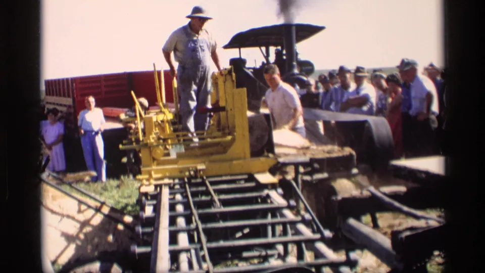 A wider 1969 Mabel, Minnesota home-movie view shows the operator, yellow machinery, logs, red wagon, and onlookers.