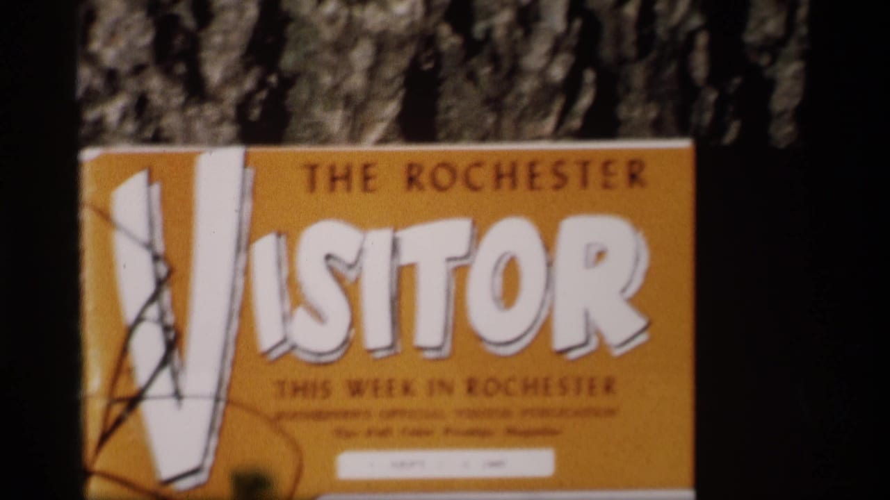 A yellow sign for The Rochester Visitor appears near the festival area, with smaller publication text partly readable and partly obscured.