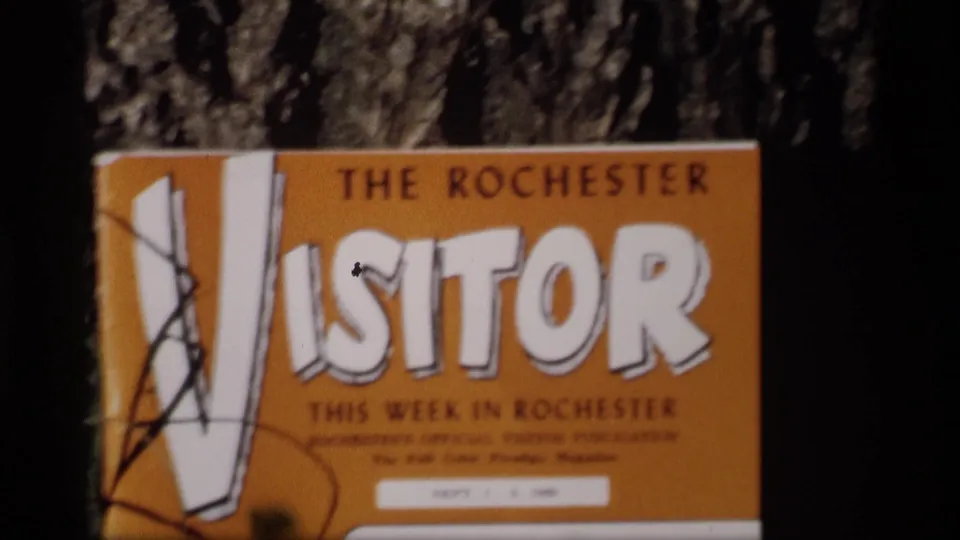1969 Mabel, Minnesota home-movie frame showing a soft-focus close-up of The Rochester Visitor cover with bold lettering.