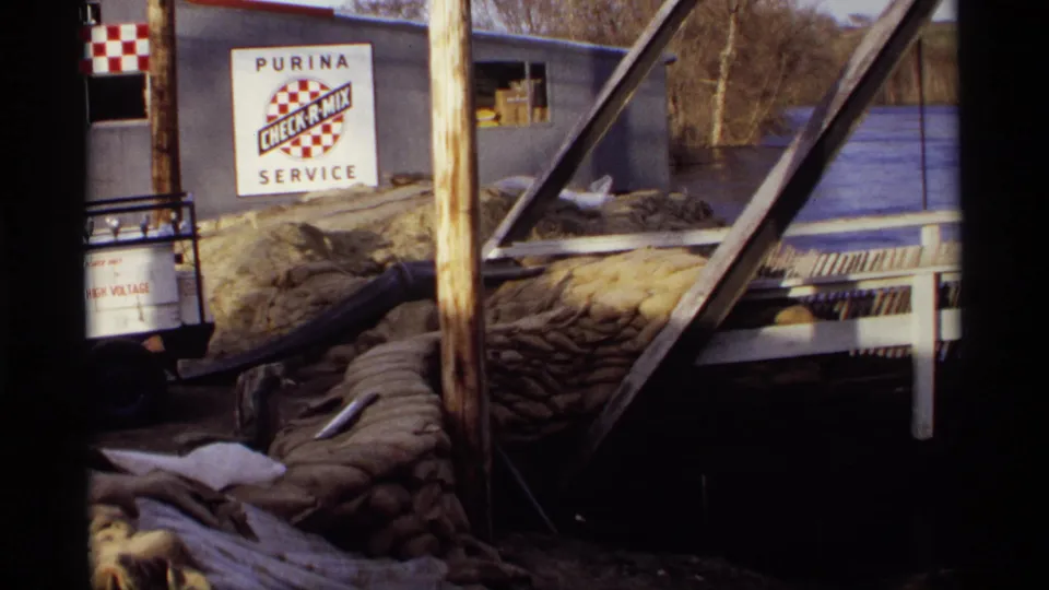 1969 Rockford, Minnesota frame showing a Purina Check-R-Mix Service building beside floodwater, sandbags, poles, and a small cart.