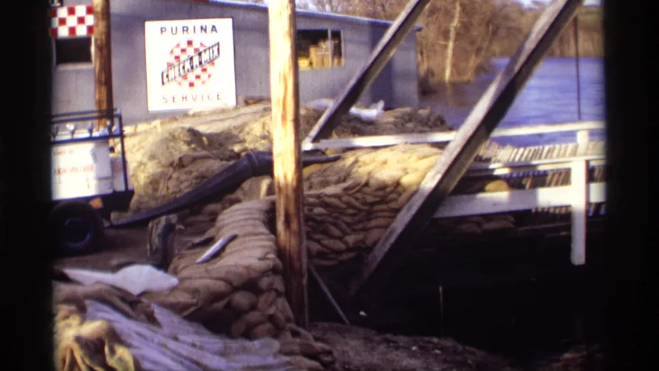 1969 Rockford, Minnesota frame of a flood scene at a Purina Check-R-Mix Service building with sandbags and high water visible.