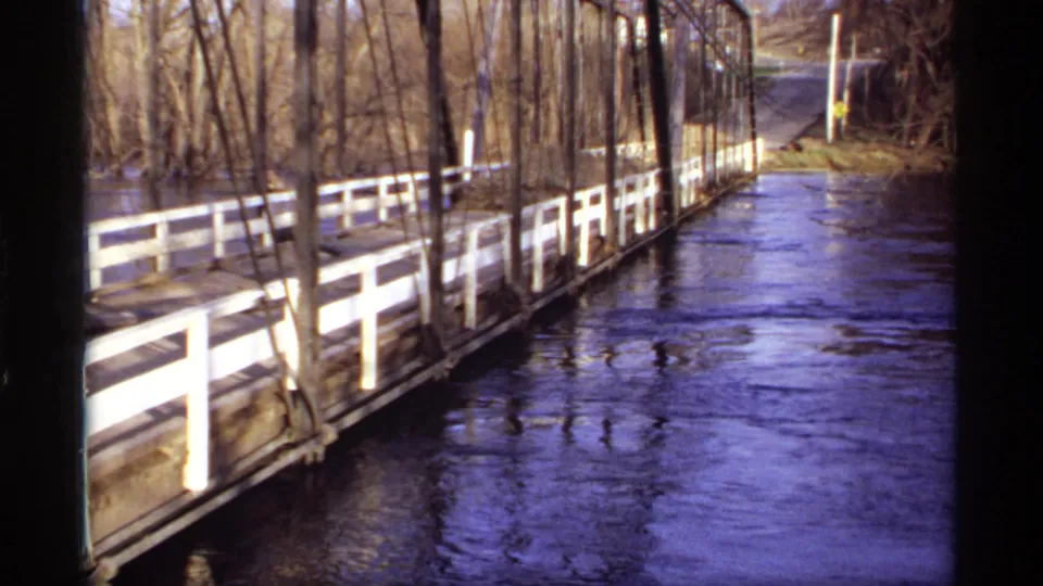 1969 Rockford, Minnesota 8mm frame showing a wooden truss bridge and white railings along a high, fast-moving river.