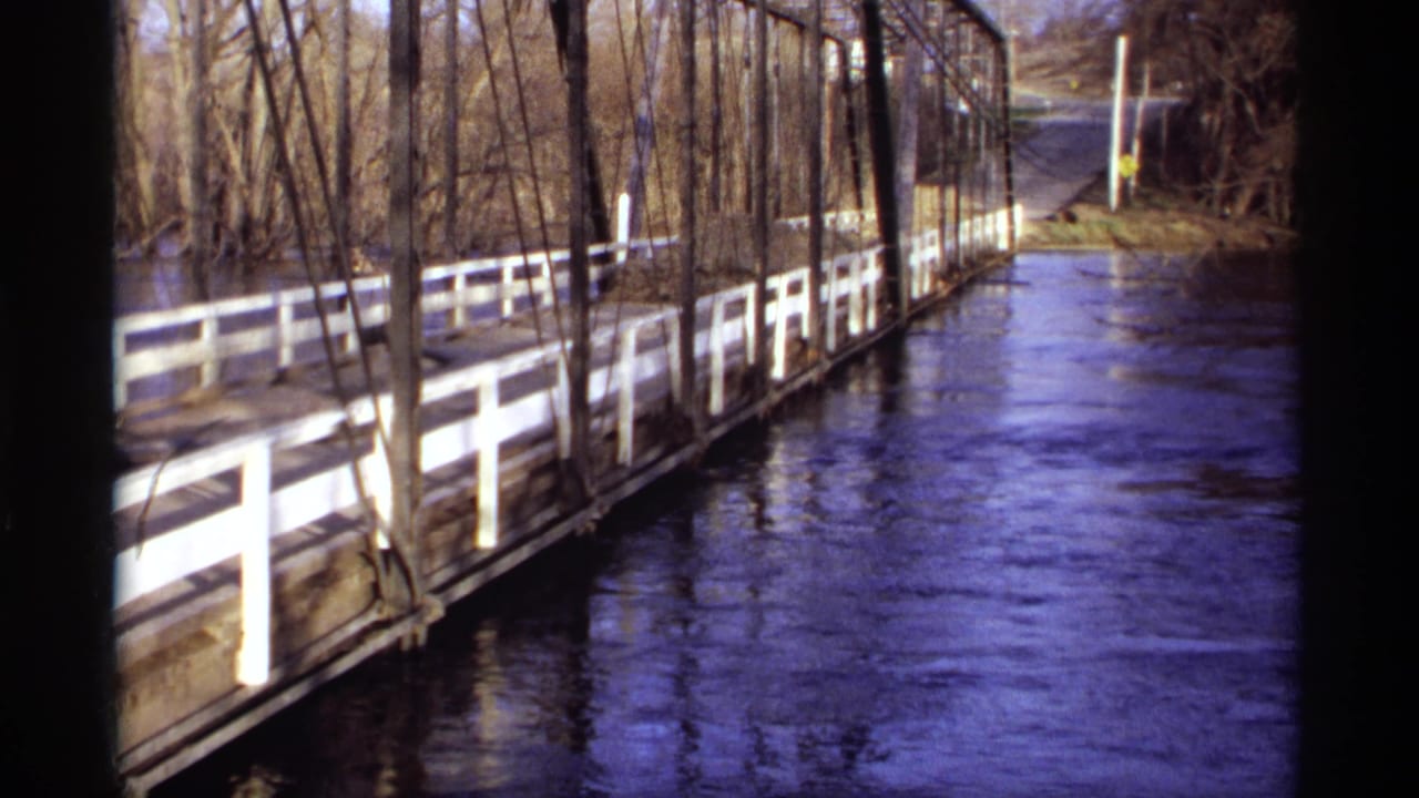 River flowing beside a white-railed bridge with bare trees along the bank.