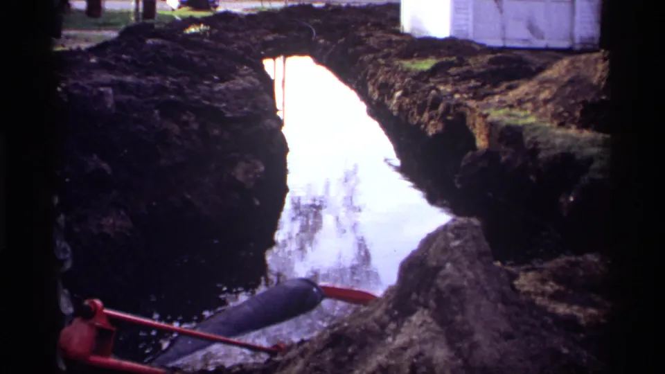 1969 Rockford, Minnesota 8mm frame showing reflective trench water, dark earth banks, and a red-handled tool near the lower edge.
