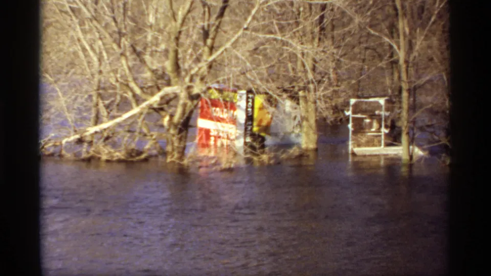 1969 Rockford, Minnesota flood scene with bare trees, a red sign partly underwater, and a small white structure at the waterline.