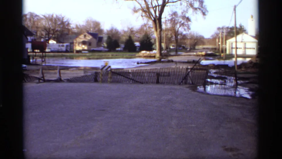 1969 Rockford, Minnesota frame showing standing floodwater near houses, fencing, leafless trees, and a road or driveway.