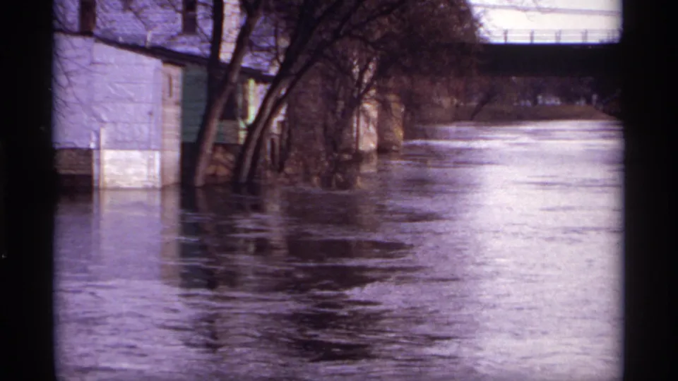 The 1969 Rockford, Minnesota flood scene shows a swollen river beside a house, bare trees, and a bridge structure.