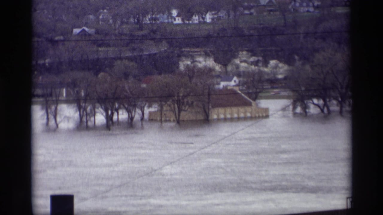 1969 Saint Paul 8mm view of floodwater around leafless trees and a low building, seen from an elevated position.