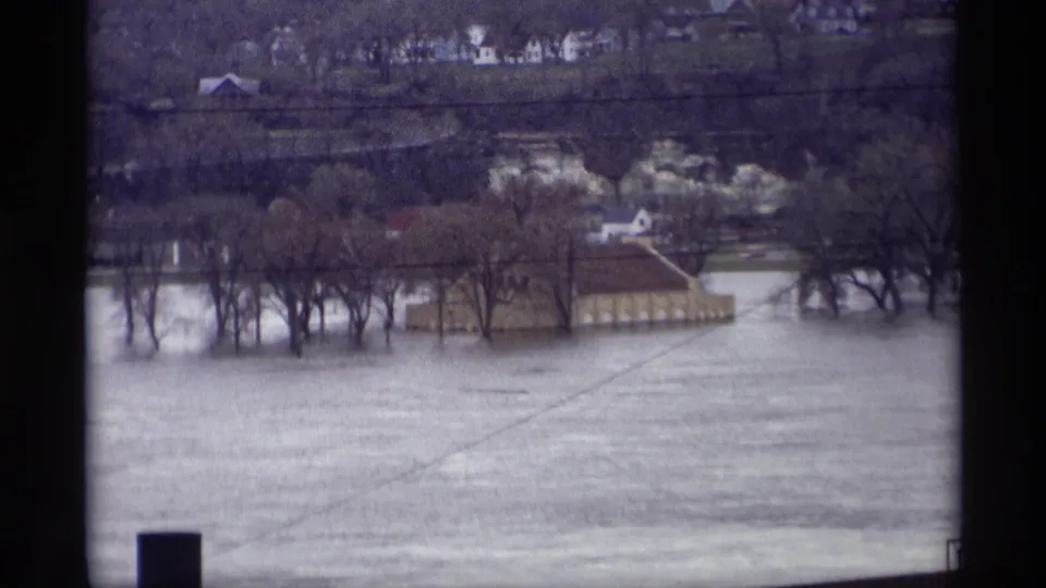1969 Saint Paul 8mm view of floodwater around leafless trees and a low building, seen from an elevated position.