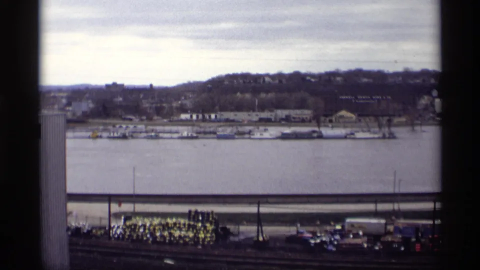 Wide 1969 Saint Paul riverfront view showing boats, shoreline structures, high water, and distant hills under an overcast sky.