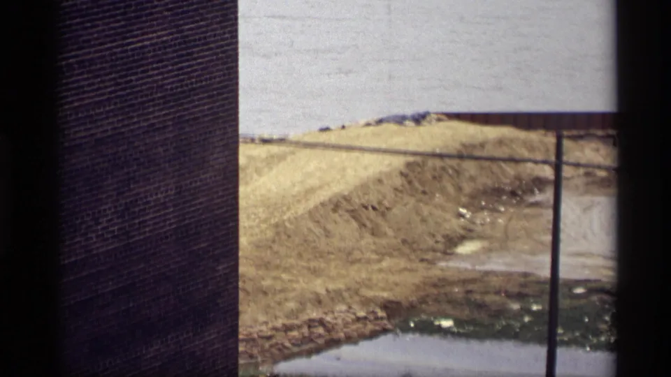 Closer 1969 Saint Paul view toward the construction area, with a brick wall, pale river water, sand pile, utility pole, muddy ground, and nearby tracks.