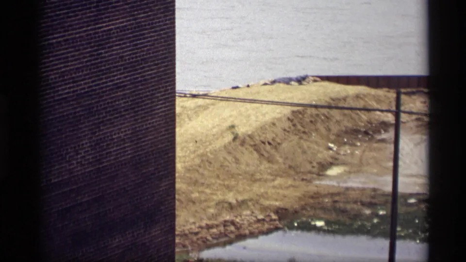 1969 Saint Paul construction foreground by the Mississippi River, showing a brick wall, sand pile, utility pole, muddy ground, and pale water beyond.