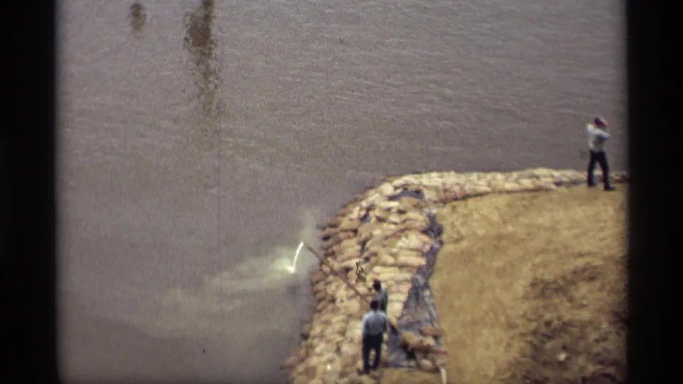 Adult men work along a stone-lined Saint Paul riverbank as hose spray hits the muddy water below.