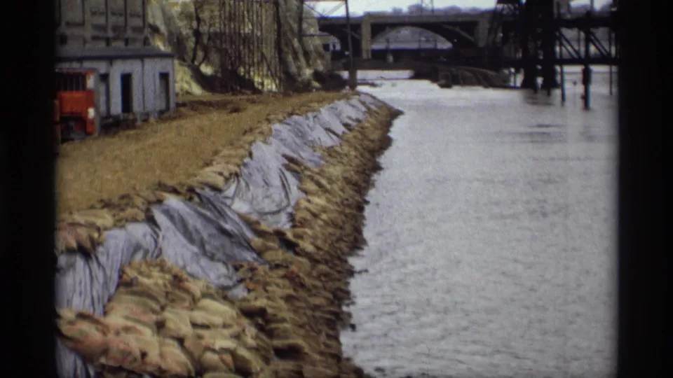 1969 Saint Paul riverfront view with sandbags, dark bank sheeting, industrial structures, and bridges spanning the water.