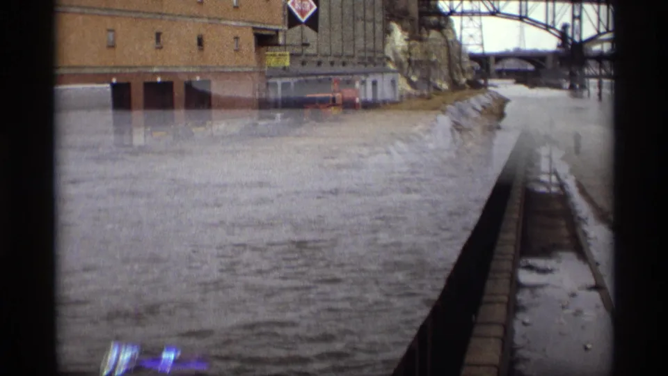 Saint Paul river scene with industrial buildings, bridgework, reinforced bank area, and film reflection or exposure overlap near the water.