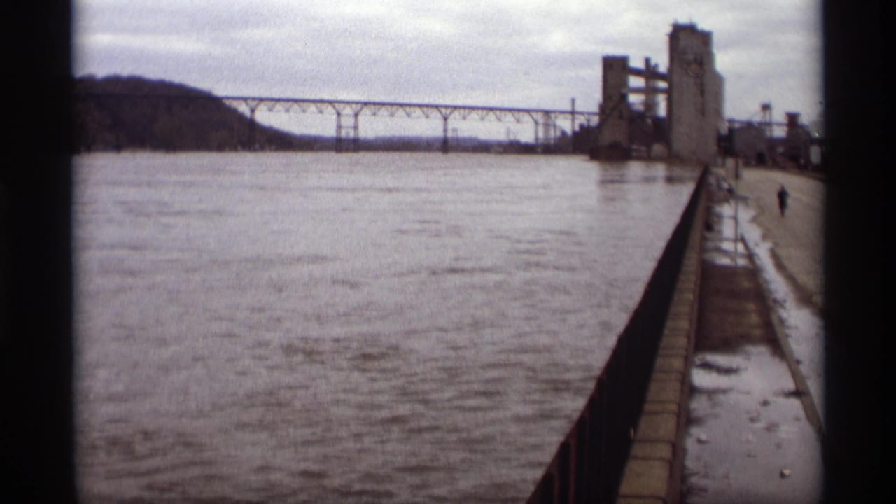 River, bridge span, industrial structure, railing, wet walkway, and distant lone person.