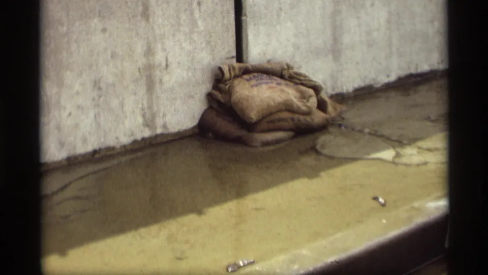 Sandbags stacked at the base of a concrete wall in the 1969 Saint Paul flood footage, with water covering the pavement.