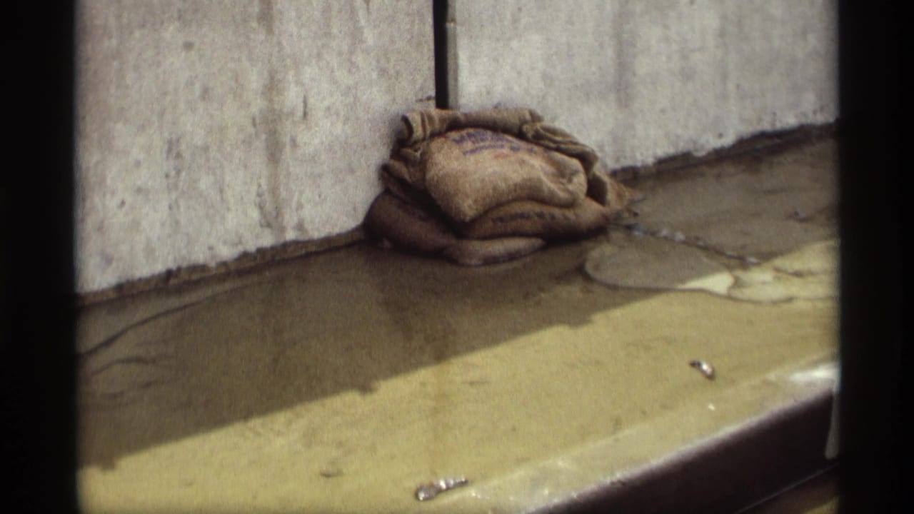 1969 Saint Paul 8mm frame showing weathered sandbags beside a leaking concrete barrier and shallow water on pavement.