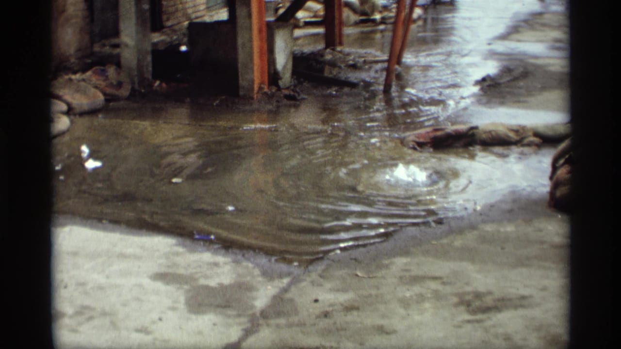 Small bubbling ripple in shallow water beside concrete and scattered debris.