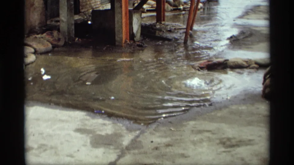 1969 Saint Paul 8mm frame showing shallow rippled water over concrete, with vertical supports, dark film borders, and debris nearby.