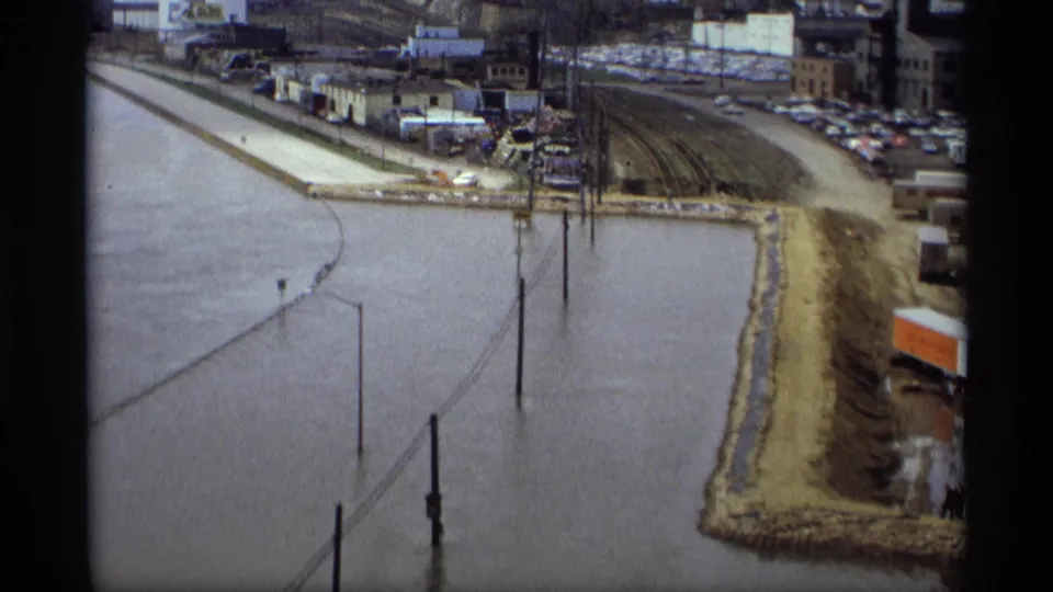 Saint Paul, Minnesota flood scene from 1969 showing muddy water around streetlights, utility poles, rail tracks, and a levee near industrial buildings.