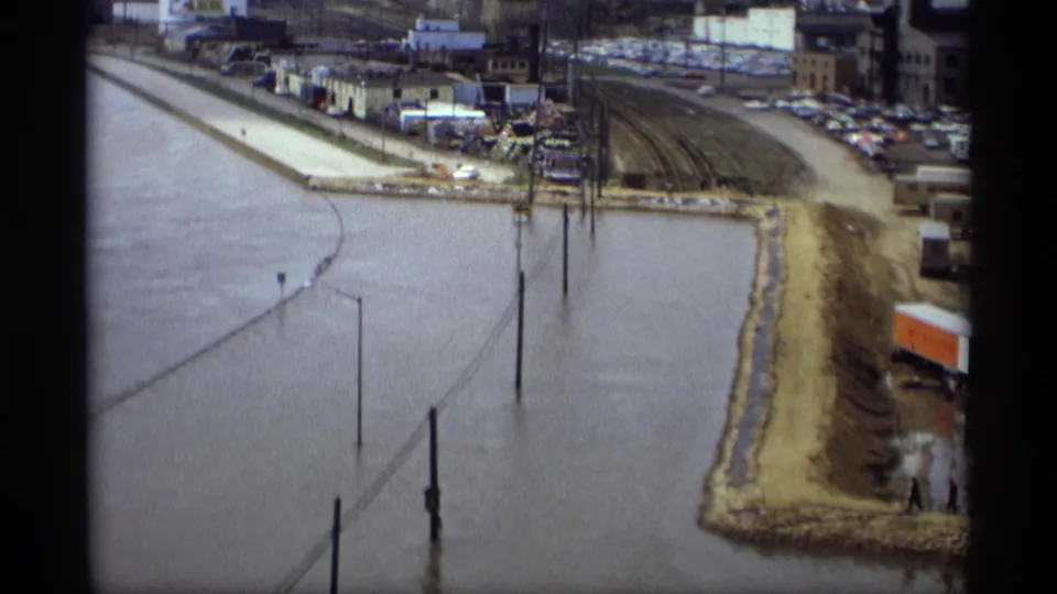 Elevated 1969 Saint Paul view of floodwater reaching a levee, with rail tracks, parked cars, utility poles, and industrial structures in the background.