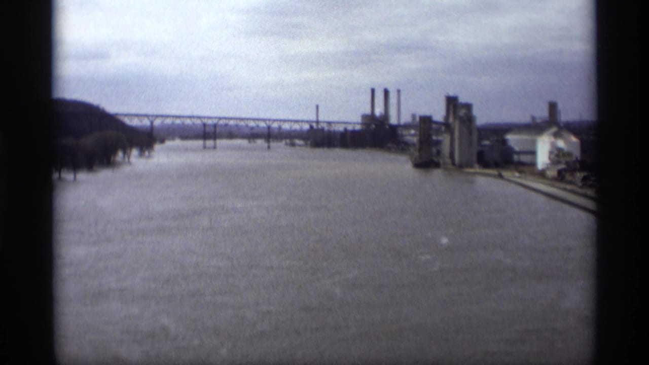 1969 Saint Paul 8mm view of a swollen river beside industrial buildings, smokestacks, and a long bridge.