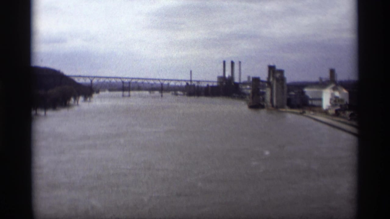 Wide river view with bridge crossing, factory structures, smokestacks, and flooded waterfront.