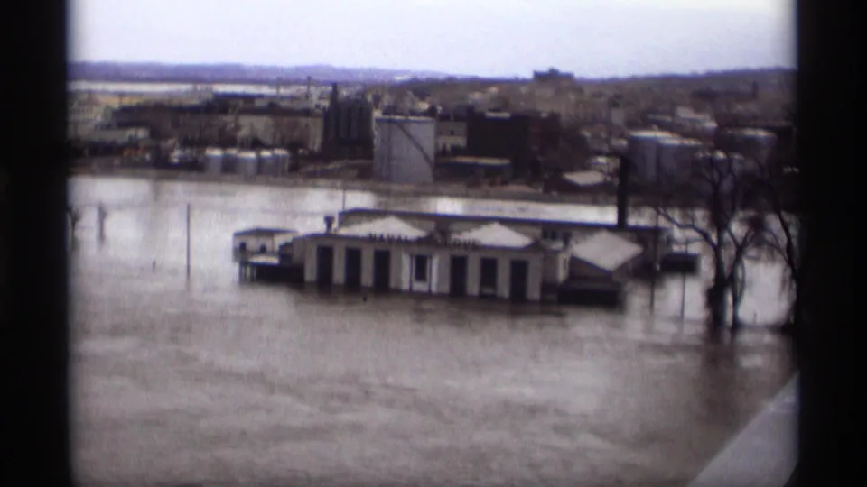 1969 Saint Paul 8mm view of floodwater around small waterfront buildings with industrial structures beyond.