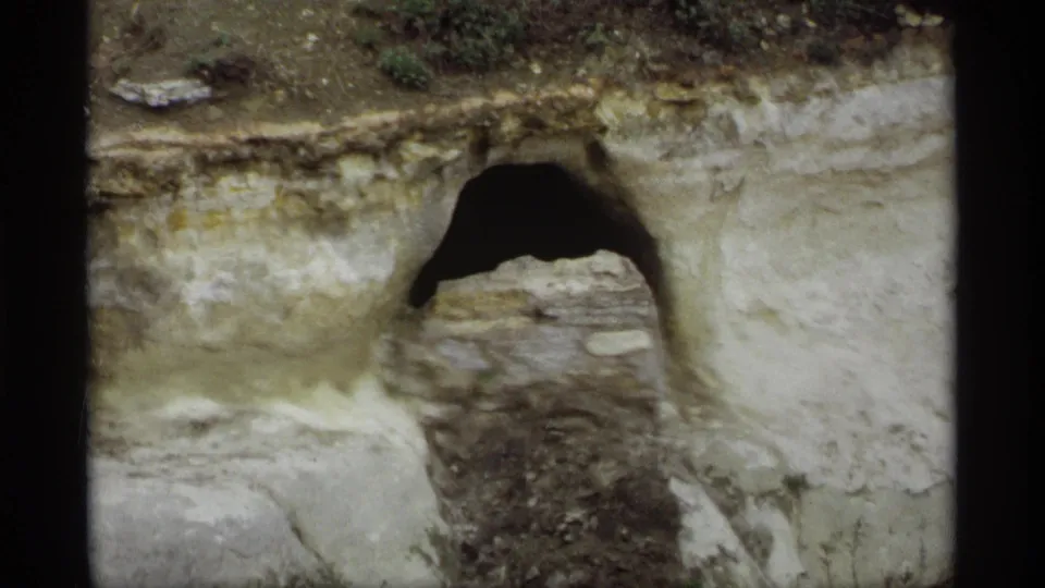 Final 1969 Saint Paul frame showing the dark arched opening set into an eroded riverbank with stone and pale soil around it.