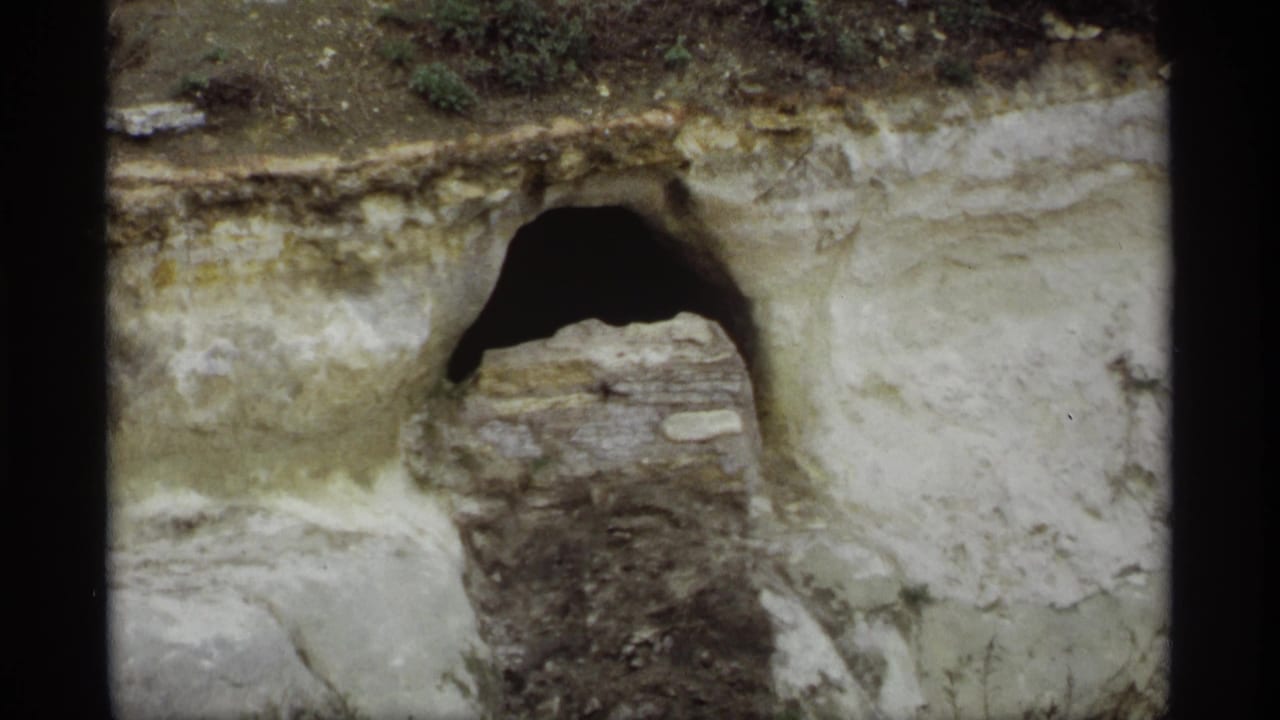 1969 Saint Paul 8mm frame showing a rocky cliff face or bank with a dark arched opening and layered stone or soil.
