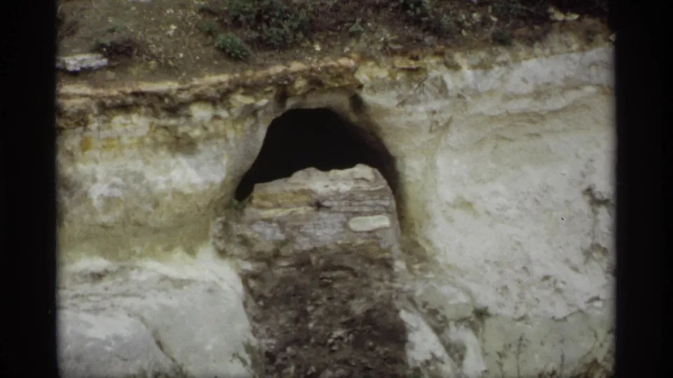 1969 Saint Paul 8mm frame showing a rocky cliff face or bank with a dark arched opening and layered stone or soil.
