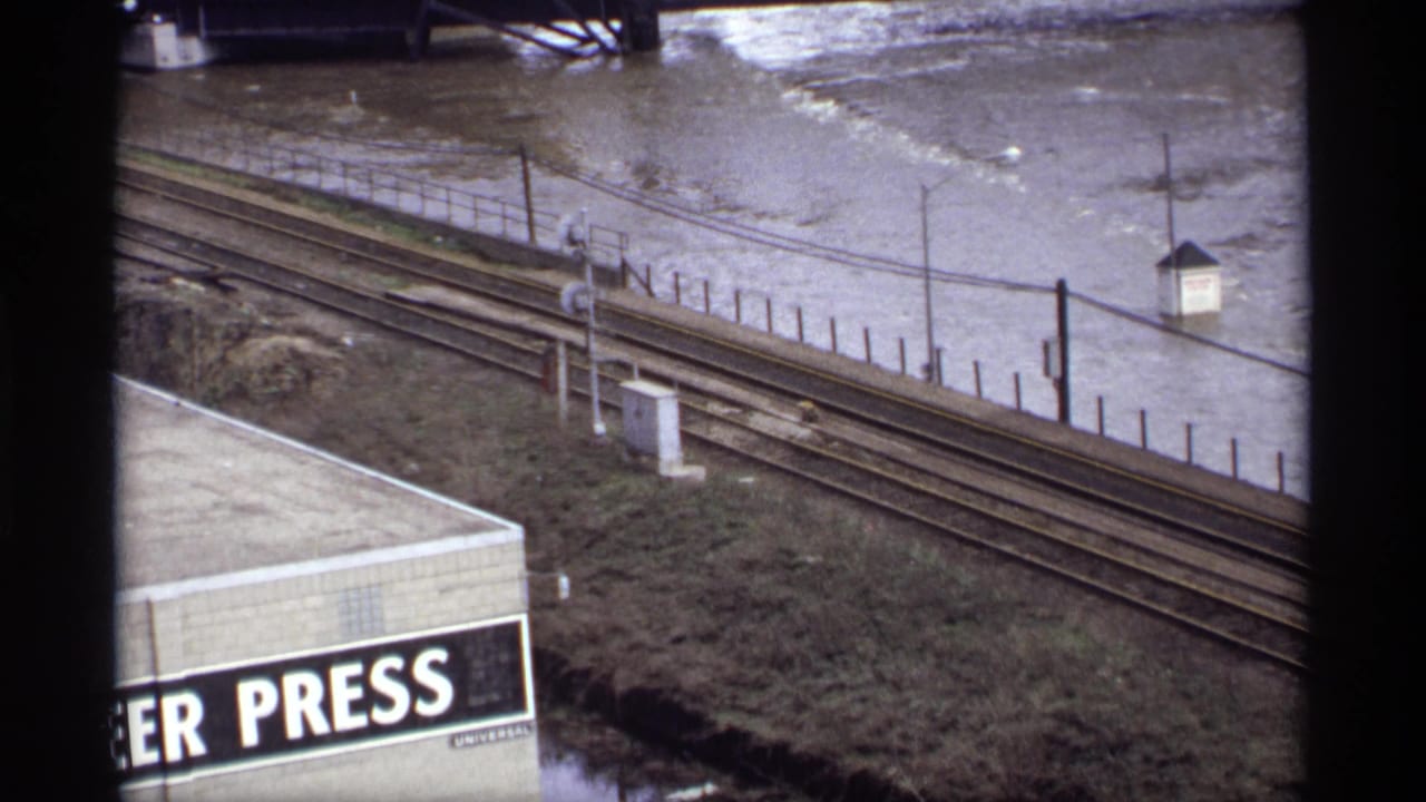 Railroad tracks beside high floodwater, with a partial PRESS sign in the foreground.