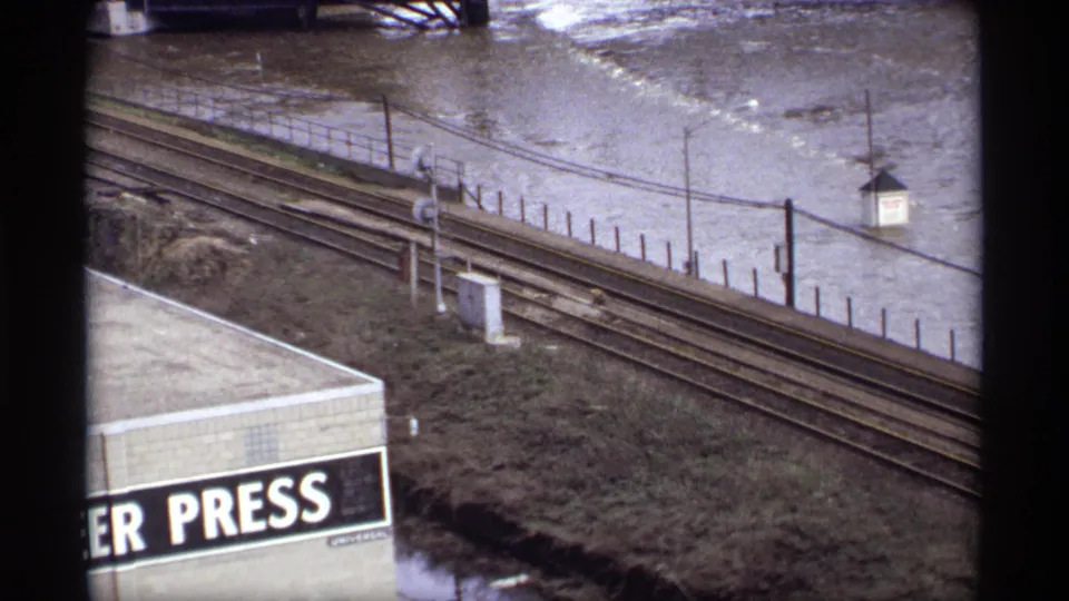 Elevated 1969 Saint Paul view of floodwater around a small riverside structure near railroad tracks, poles, and a partial PRESS sign.