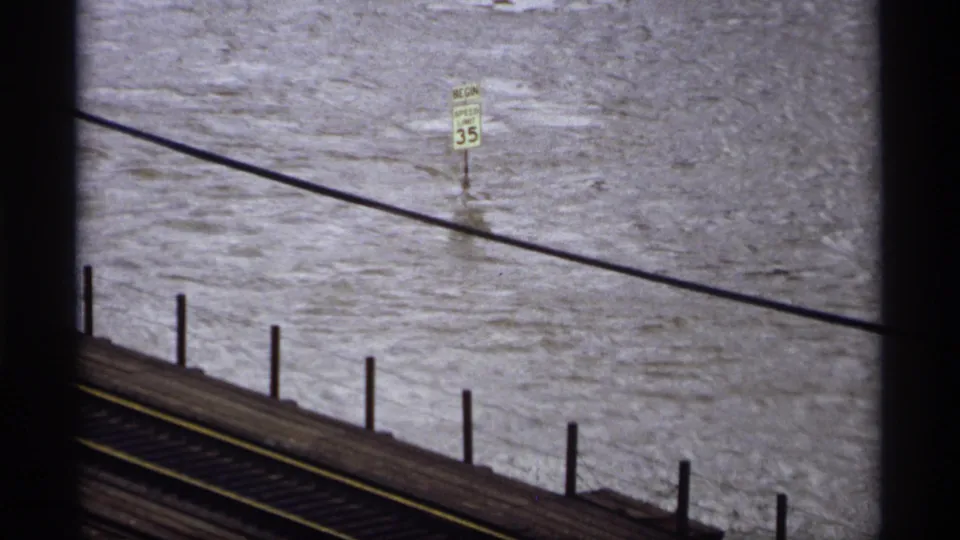 A 35 mph road sign stands in floodwater near a bridge or rail structure in 1969 Saint Paul, Minnesota footage.