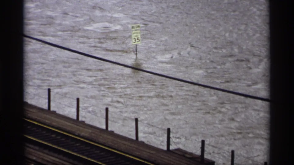 Saint Paul 1969 flood scene with murky water, a speed limit sign, railroad tracks, and a utility wire crossing the view.
