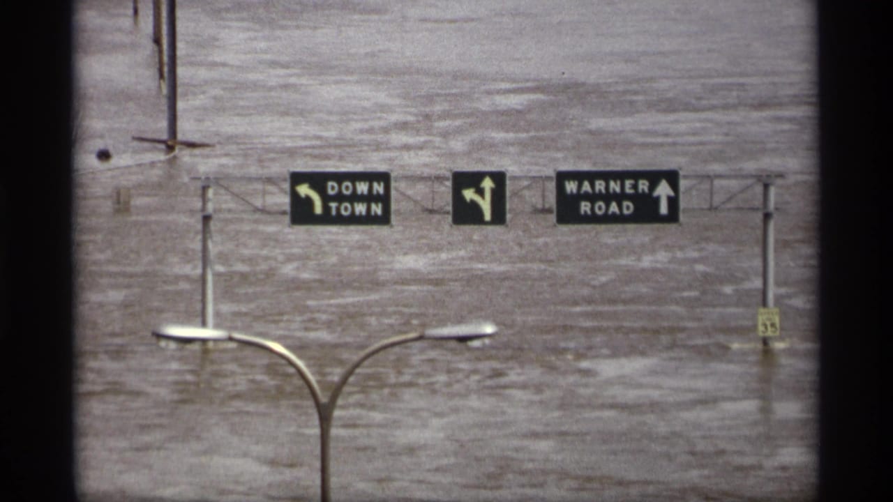 Overhead downtown and Warner Road signs above flooded roadway area.