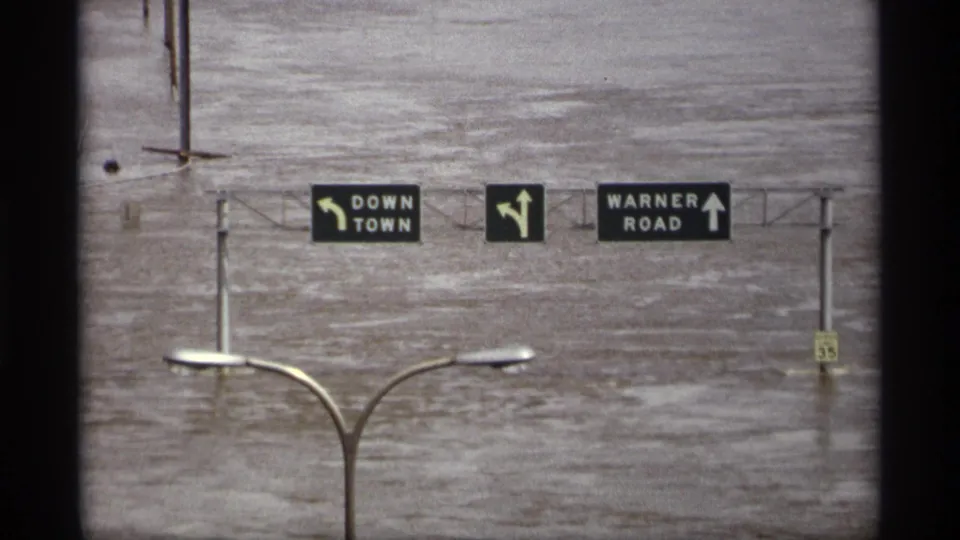 Saint Paul, Minnesota flood view with downtown and Warner Road signs suspended over broad floodwater.