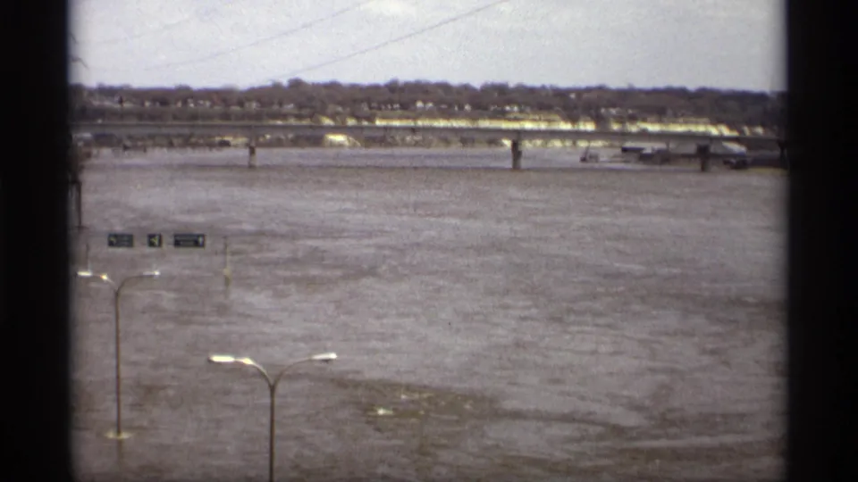 Wide 1969 Saint Paul flood view across high water toward a bridge and far-bank buildings, with signs and streetlights partly in the foreground.