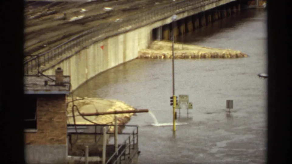 1969 Saint Paul flood view of a concrete bridge approach, submerged road signs, streetlights, a brick structure, and high river water.