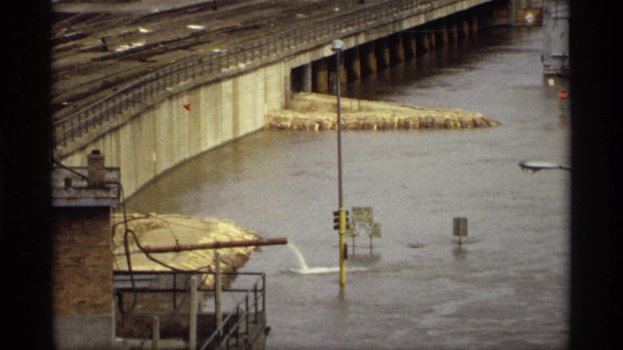 1969 Saint Paul flood footage showing high water around a concrete bridge approach, railings, street signs and a yellow traffic pole.