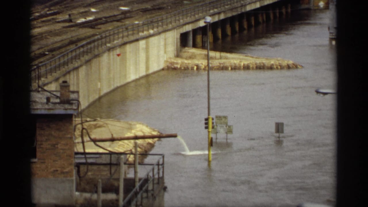 High water surrounds bridge supports, signs and a partially submerged traffic pole.