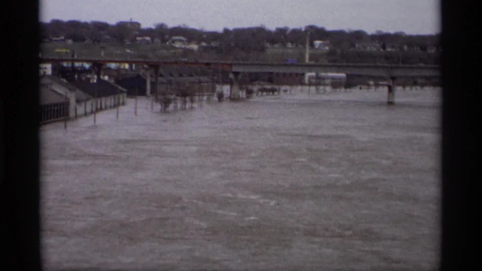 Wide Saint Paul flood view from 1969, looking across high water toward a bridge, riverside structures, distant houses and bare trees.