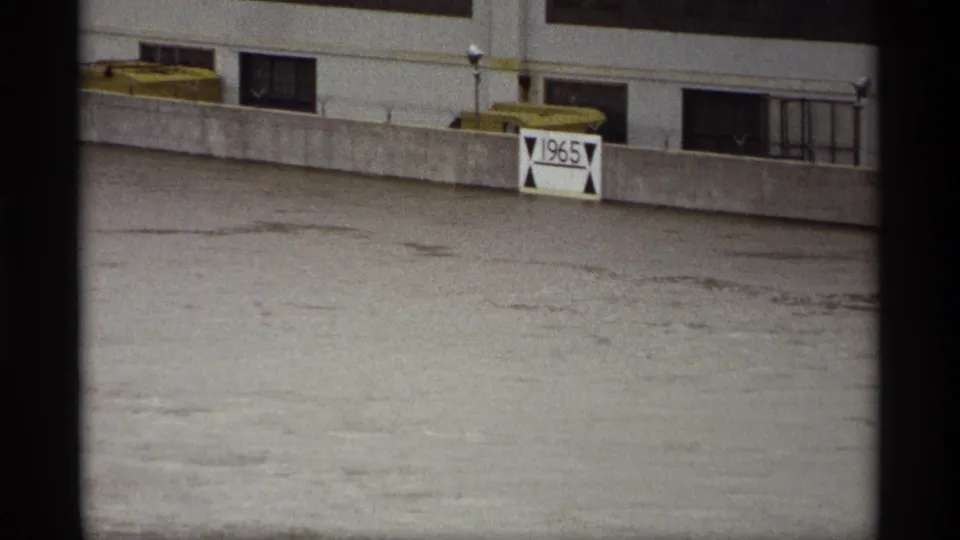 Saint Paul, Minnesota 1969 frame showing a concrete riverfront wall, windows, yellow structures, and a 1965 marker above floodwater.