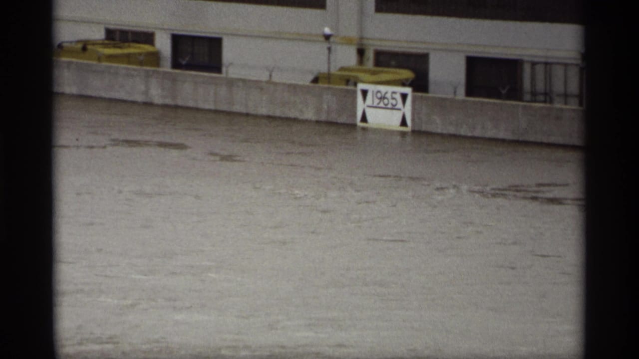 1969 Saint Paul floodwater surges past a concrete barrier, nearly submerging a white sign marked 1965.
